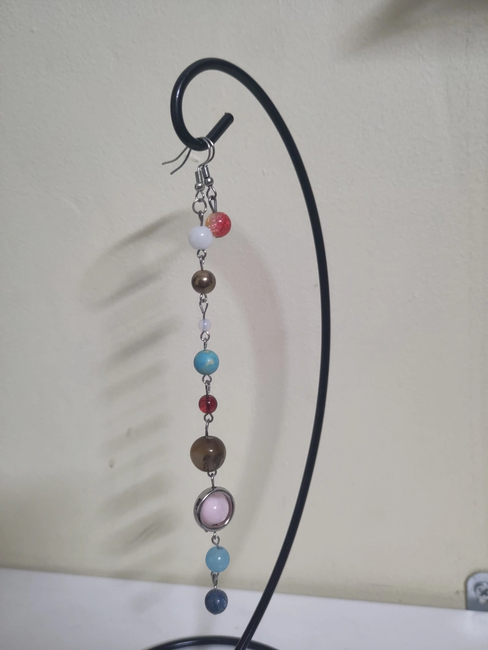 A chain of marbles on a fishhook representing the planets in the solar system with a second fishhook with just a single red and yellow marble on it representing the sun.