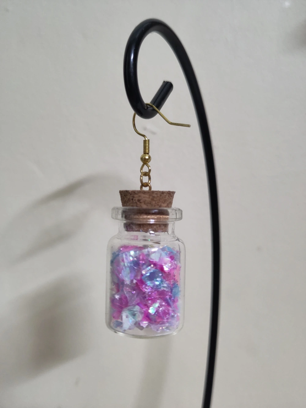 A small jar with a cork stopper filled with blue, pink and white glitter.