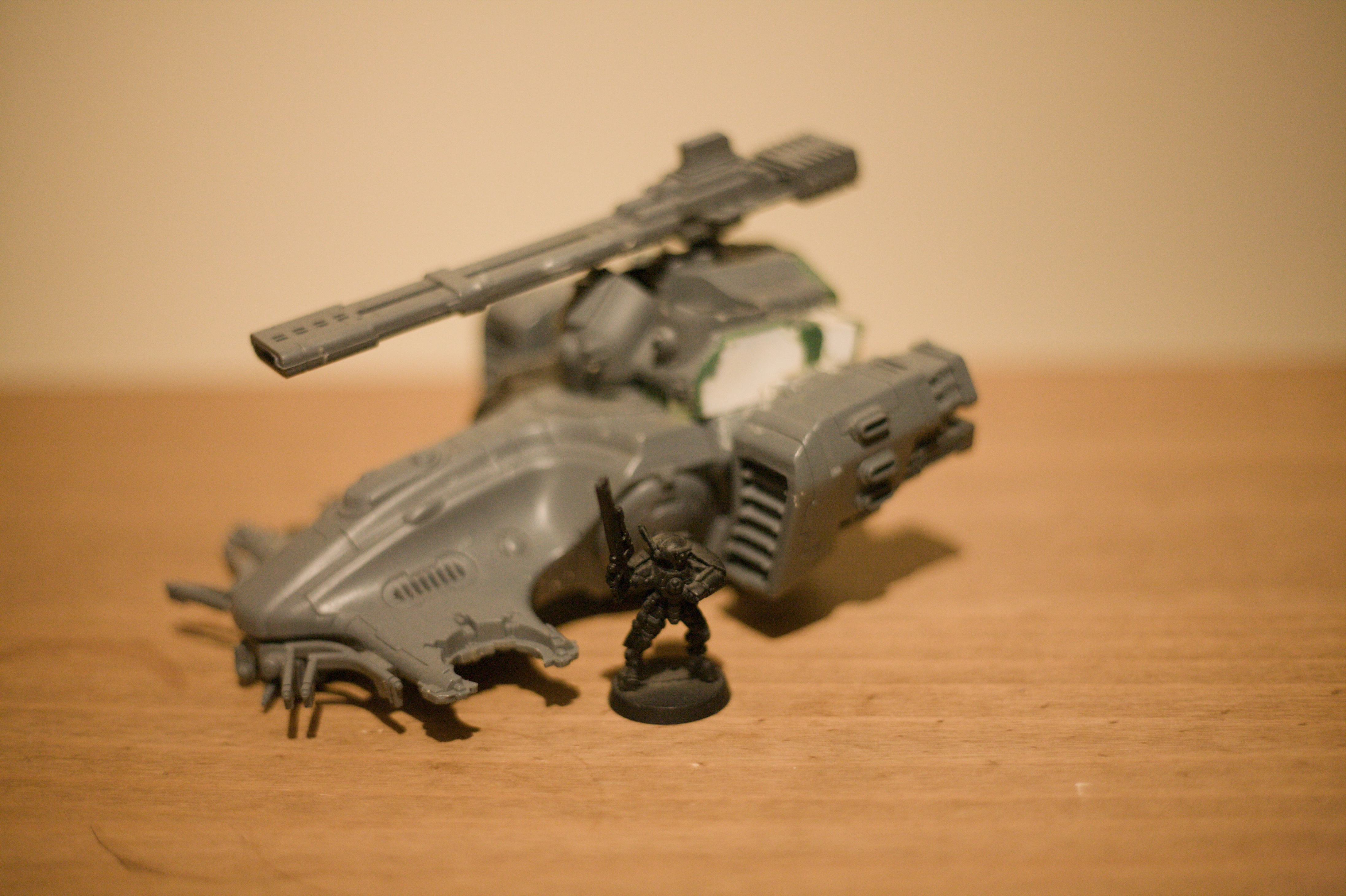 Some Warhammer miniatures. An armoured soldier painted solid black stands in front of an unpainted hover tank that’s out of focus.