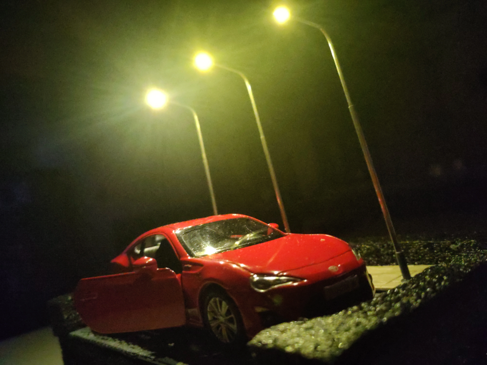 A diorama of a red Toyota GT86 illuminated by some tiny LED street lights.